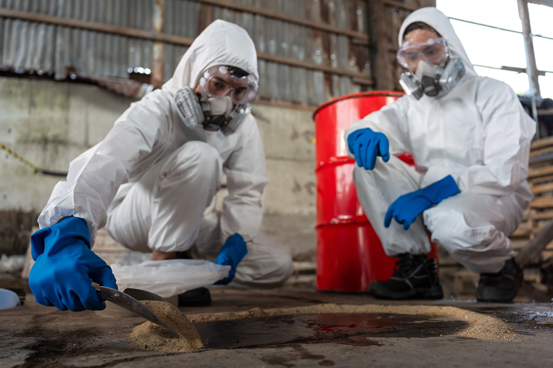 A team of two chemists, wearing PPE suits and gas masks, recover a deadly chemical spill on the factory warehouse floor. Correct disposal of chemical spills in industrial plants.